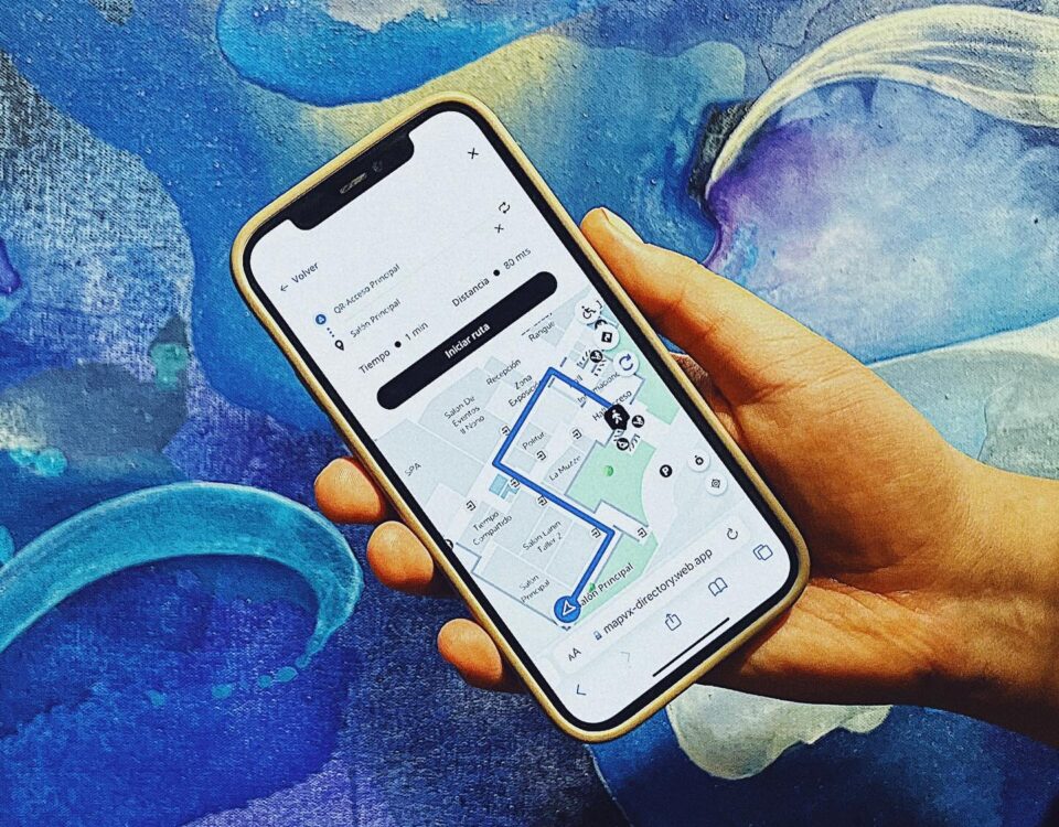 Imagen de una mano sosteniendo un celular donde se muestra la interfaz de MapVX y un recorrido dentro de un evento en Hoteles.